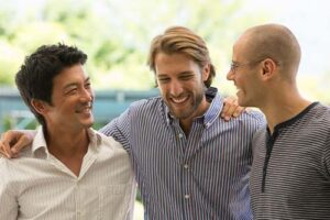 three men smiling and laughing in a group talking about mens addiciton treatment programs