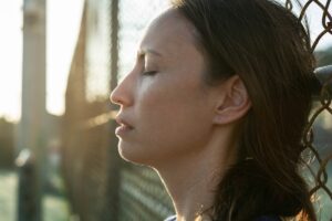 woman leaning against chain link fence outside and thoughtfully recalling commonly abused opioids