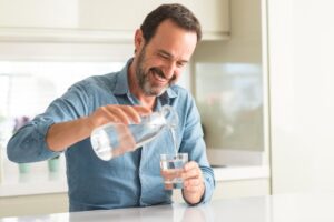 a person smiles and pours water after learning how to safely detox from alcohol at home