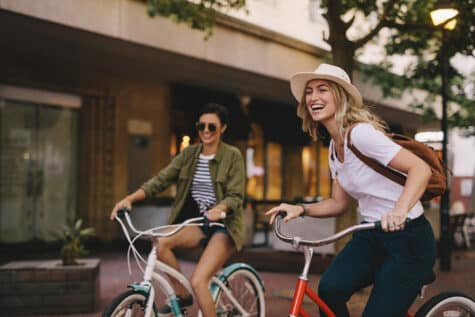 Two women ride bikes, a fun activity for a sober summer.